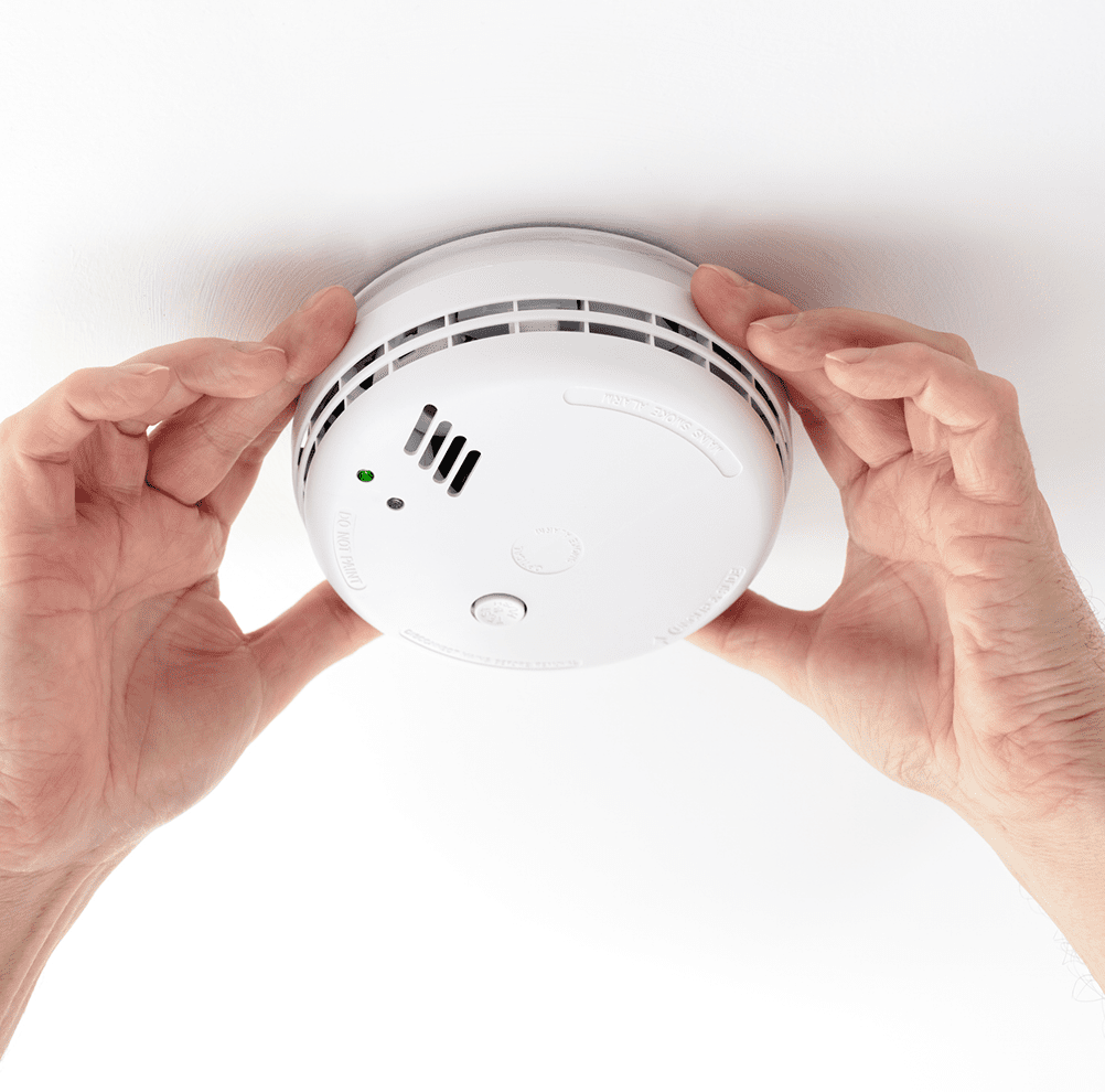 Hands installing a ceiling smoke detector.